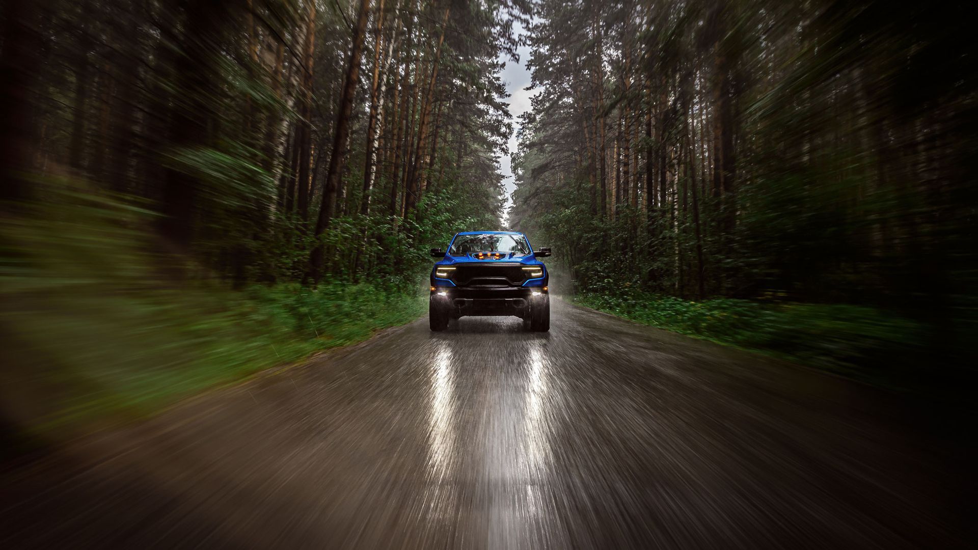 Blue truck driving on a wet road through a forest; motion blur effect.