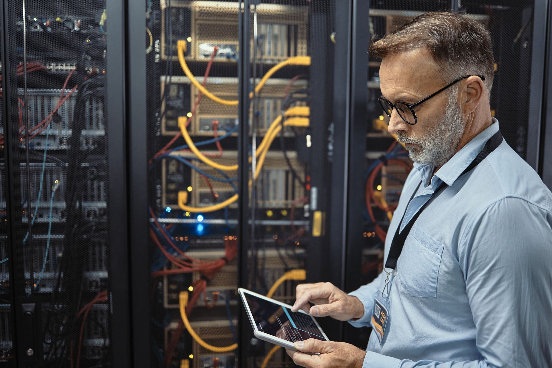 A man is using a tablet in a server room.