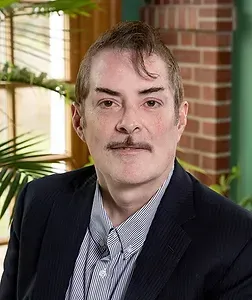 A man with a mustache is wearing a suit and striped shirt.