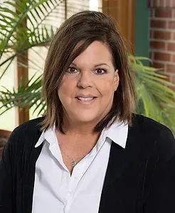 A woman in a white shirt and black jacket is smiling for the camera.