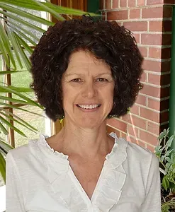 A woman with curly hair is smiling in front of a brick wall.