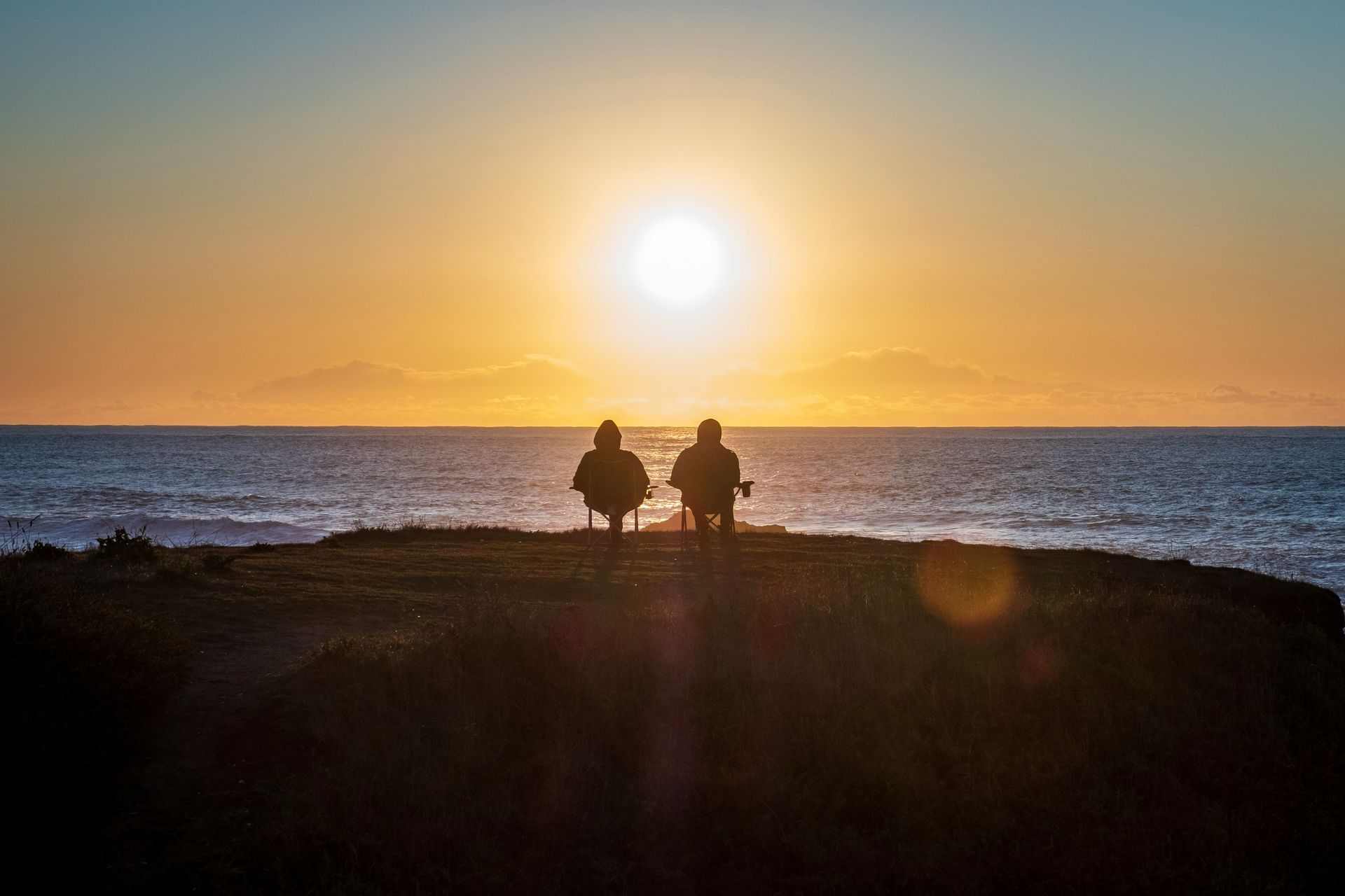 Two people are sitting on a bench overlooking the ocean at sunset.