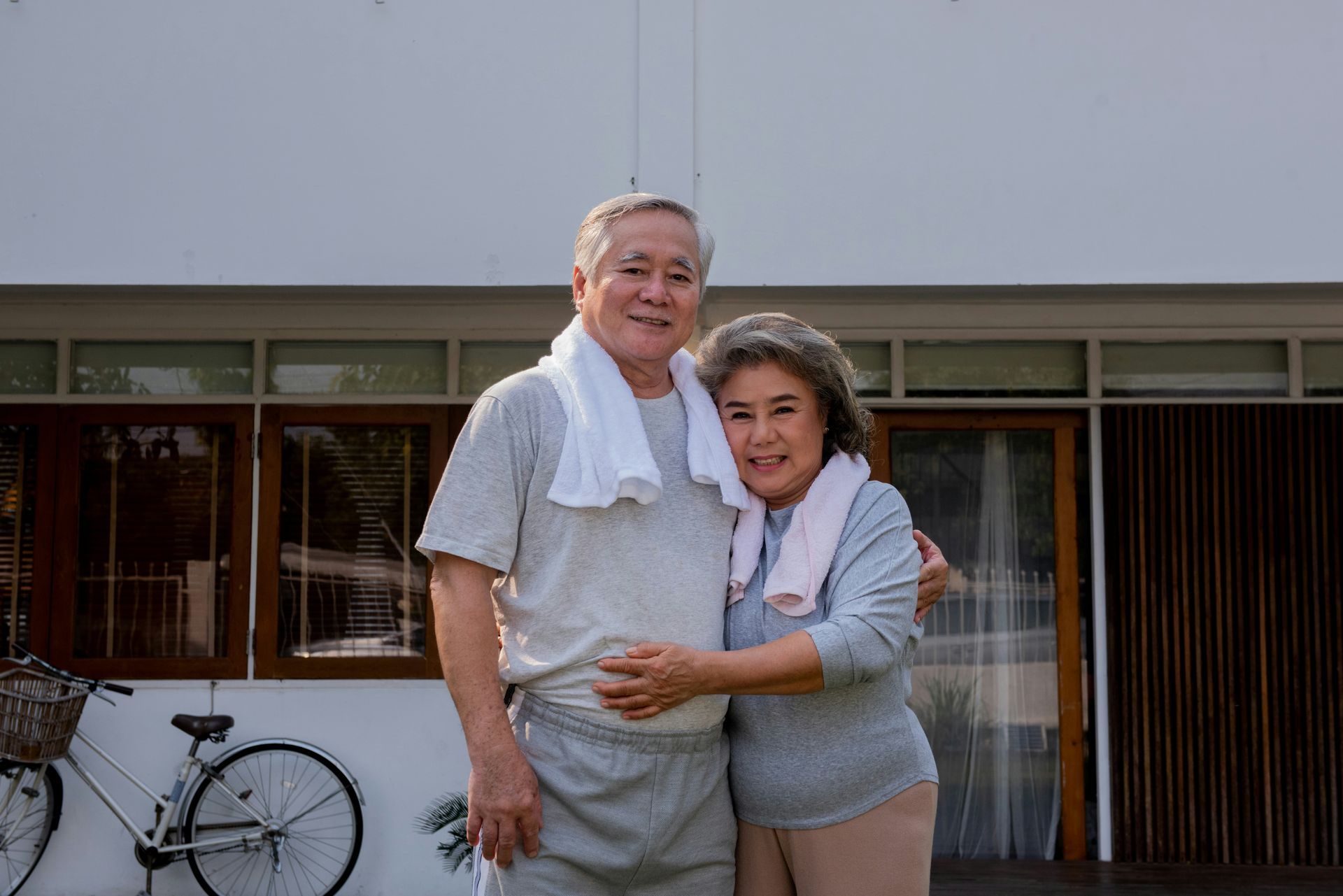 An elderly couple standing next to each other in front of a house.