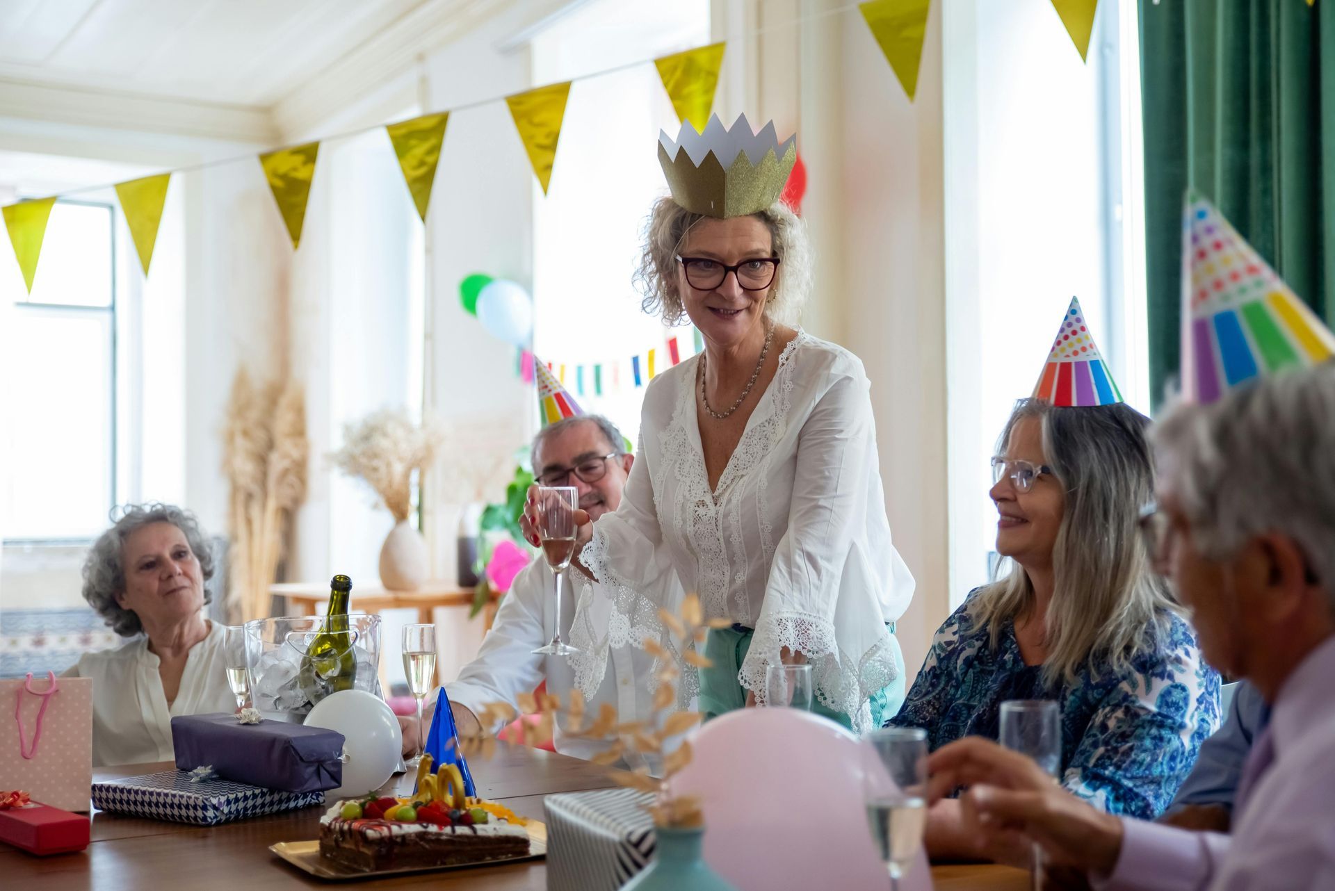 A group of elderly people are sitting around a table at a birthday party.