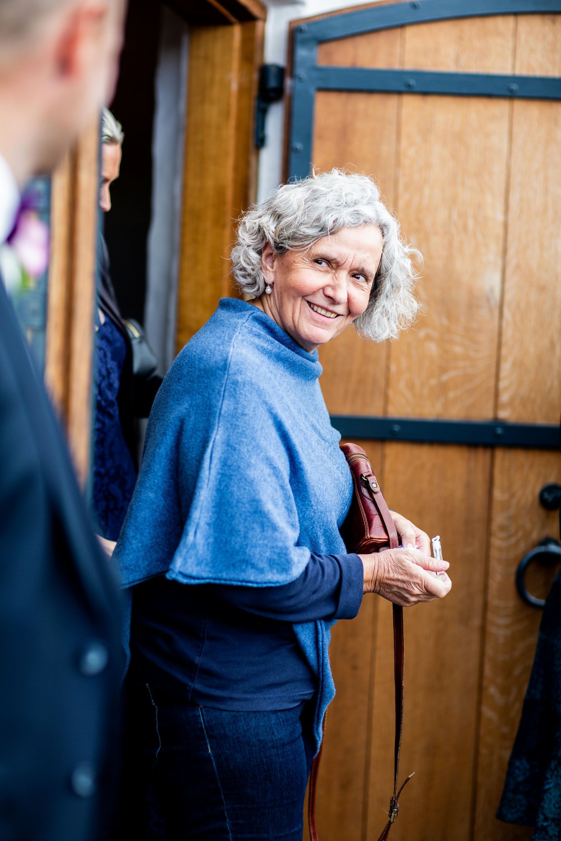 A woman in a blue poncho is standing in front of a wooden door.