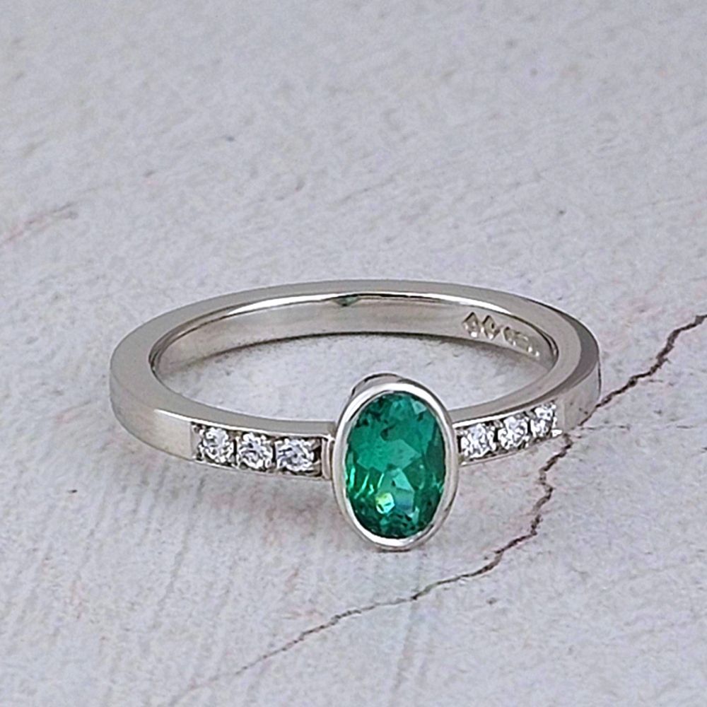 a dainty engagement ring with an oval emerald set in platinum with 3 small diamonds on each side.