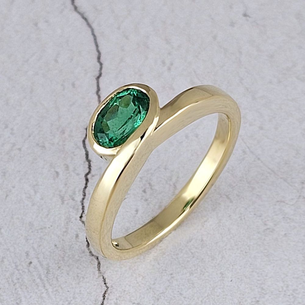 Contemporary engagement ring with an oval emarald in yellow gold
