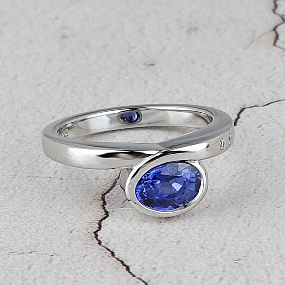 a contemporary engagement ring in platinum with an oval blue sapphire set accros the finger