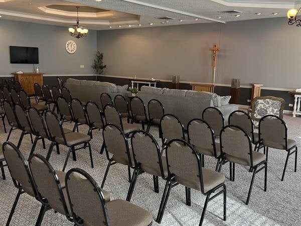 Rows of chairs face a sofa in a gray-walled event space; a TV and decorative items are visible.