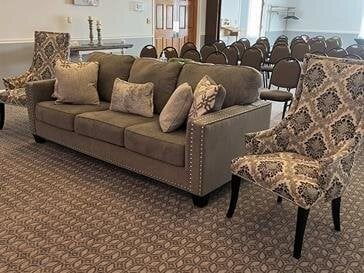 A gray sofa with throw pillows and two patterned armchairs in a room with a patterned carpet.