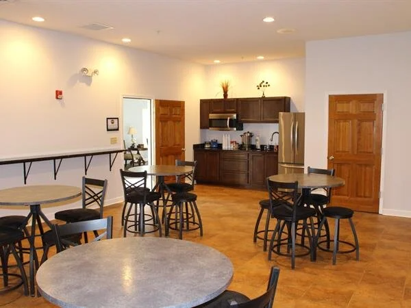 An empty cafe area with round tables, bar seating, a kitchenette, and two closed wooden doors.