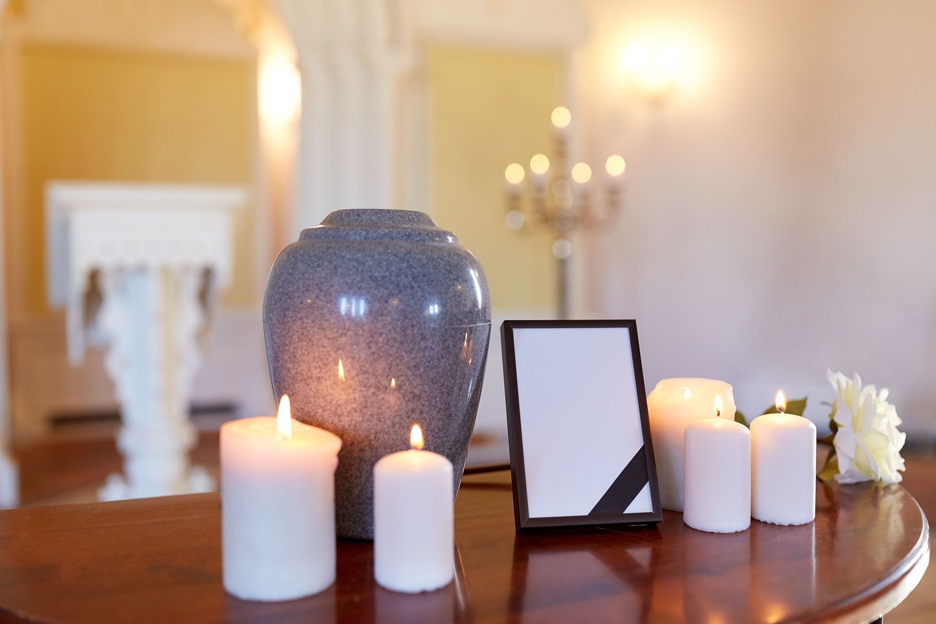 A memorial with an urn, lit candles, framed photo with a black ribbon, and white flowers on a wooden table.