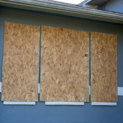 Three wood panels, attached to a blue building's exterior, covering a window.