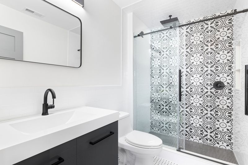 Modern bathroom with black and white patterned shower, black fixtures, and a vanity.