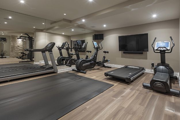 Home gym with treadmills, exercise bikes, weight machine, TV, and large mirror.