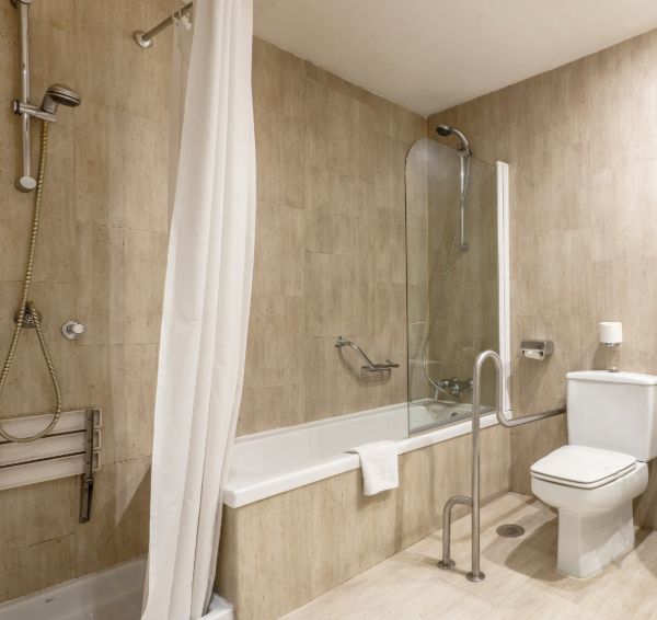 Accessible bathroom with tub, shower, grab bars, and toilet. Neutral-toned tiles and white fixtures.