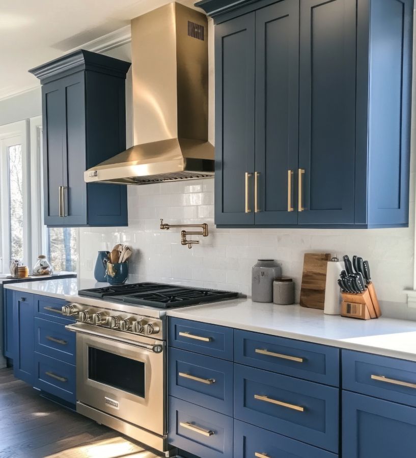 Blue kitchen cabinets with stainless steel appliances, gold hardware, and white countertops.