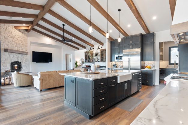 Modern kitchen with dark cabinets, large island, and open living area with exposed wood beams.