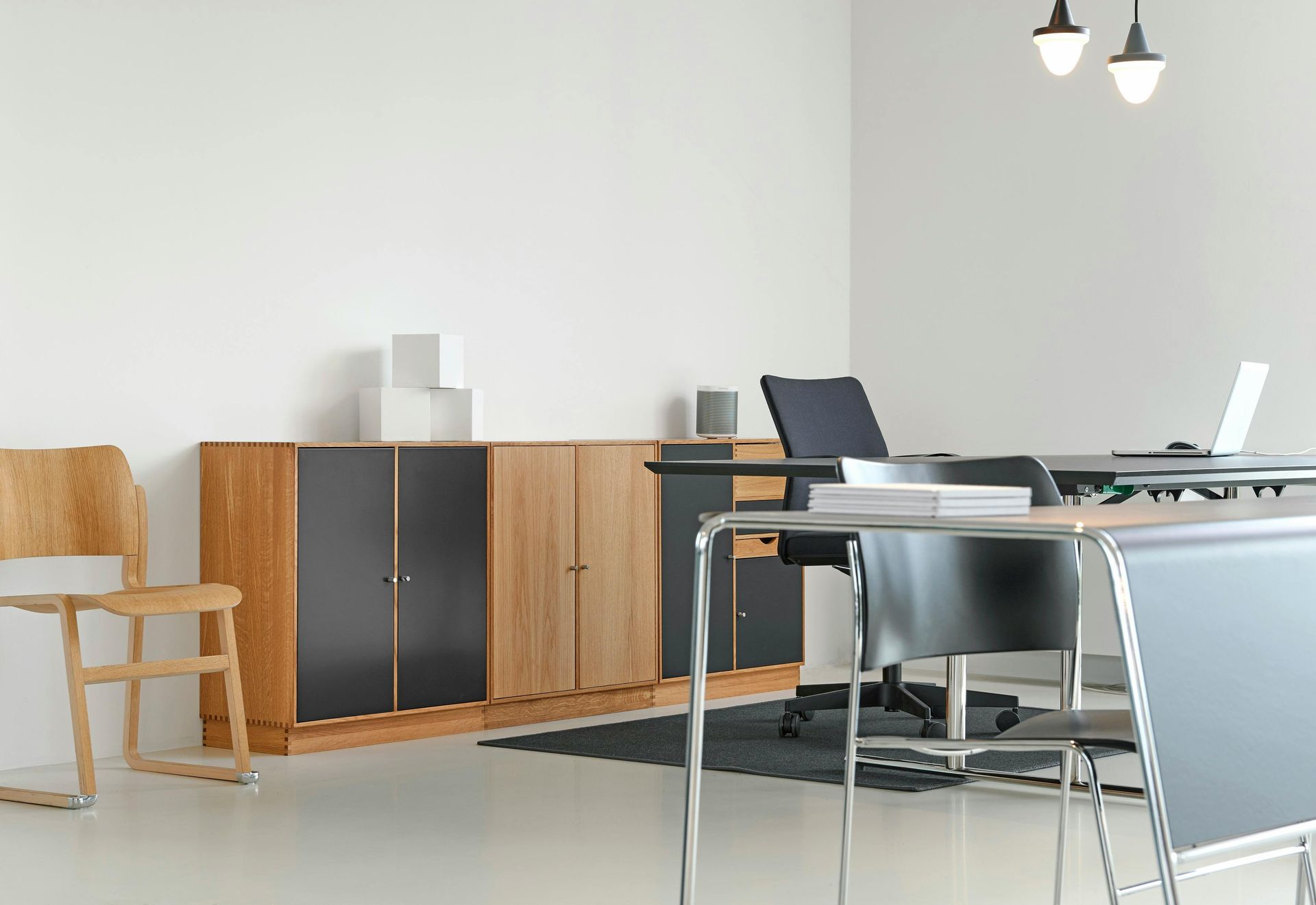 Office space: wooden cabinets, desk, chairs, and laptop, against a white wall and floor.
