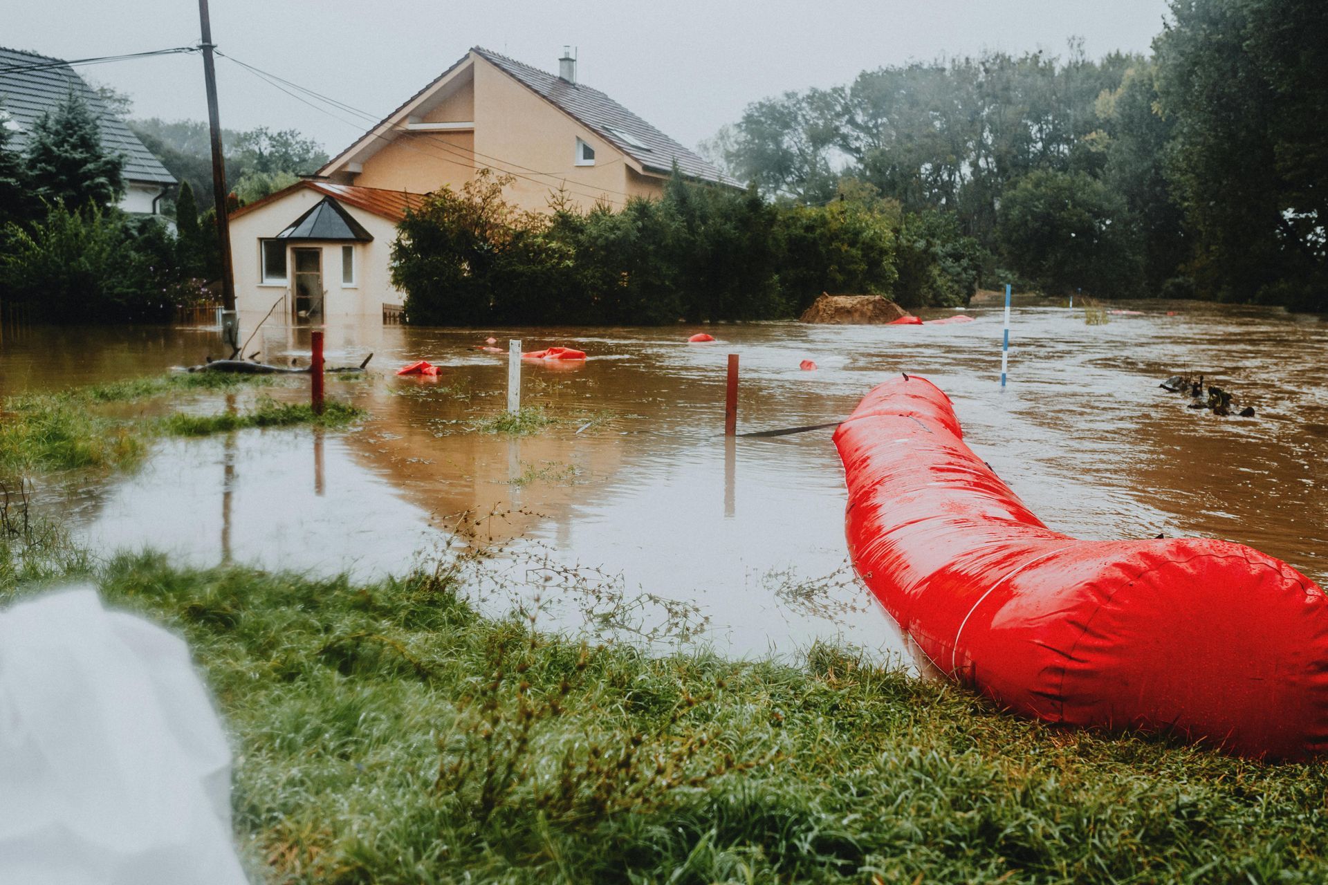 Flooded suburban neighborhood with water surrounding houses, red flood barrier in foreground.