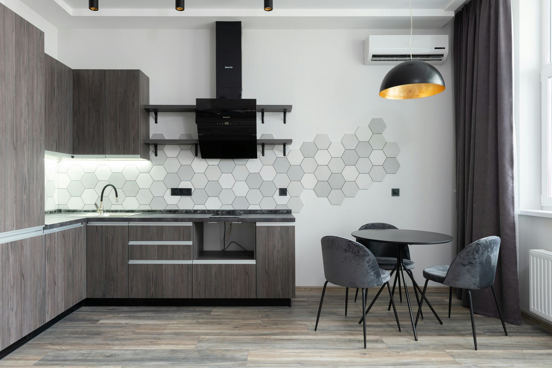 Modern kitchen with gray cabinets, hexagon tile backsplash, black hood, round table, and gray chairs.