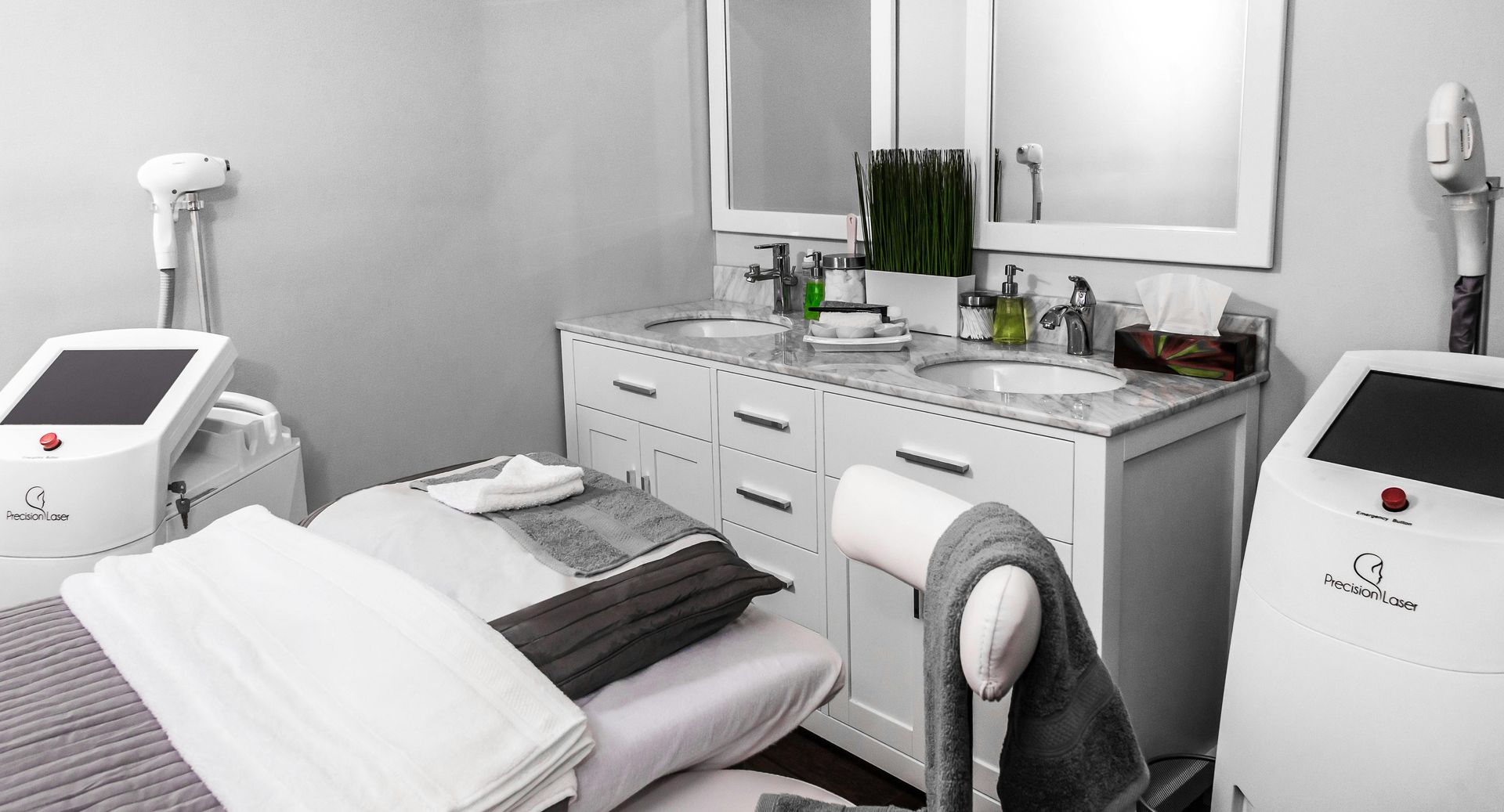 Spa treatment room with medical equipment, white cabinets, and two sinks.