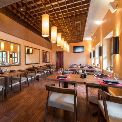 Restaurant interior with wooden tables, chairs, warm lighting, mirrors, and a grid-patterned ceiling.