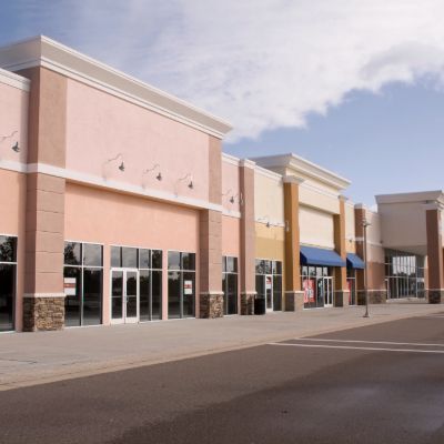 Empty commercial storefronts in a row, painted pink, beige, and cream.