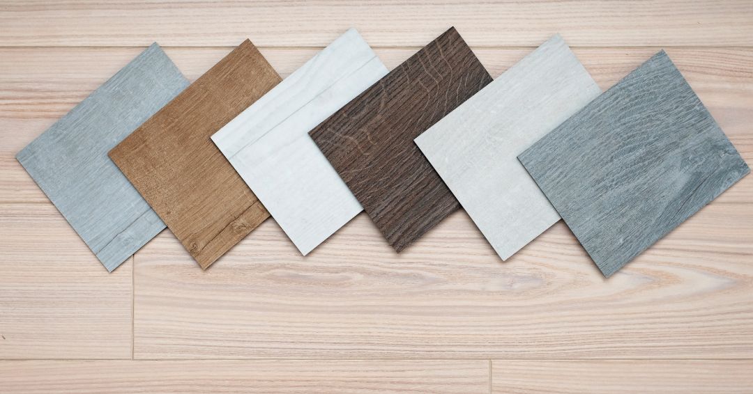 Samples of flooring tiles in various colors arranged on a light wood floor.