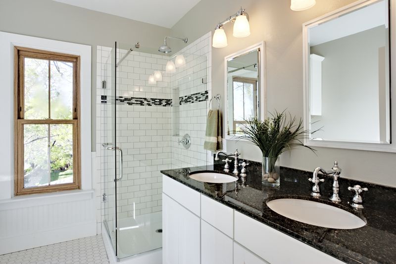 Modern bathroom with white tile shower, dual sinks, and a window.