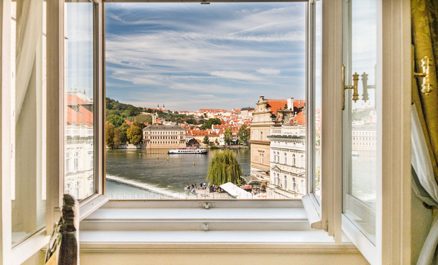 Open window overlooking Prague, Czech Republic. River, buildings, bridge, and blue sky.