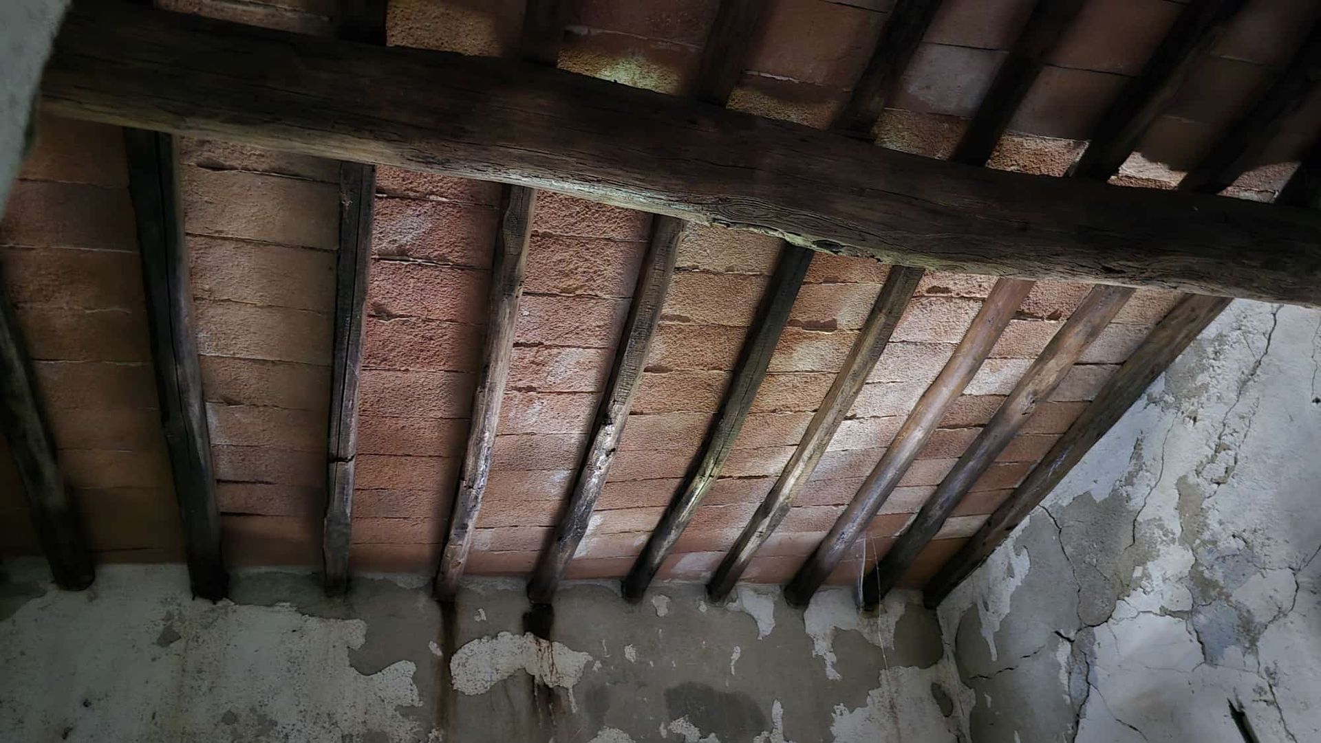 Travi in ​​legno a vista sul soffitto e tegole rossastre sopra pareti intonacate di bianco screpolato.