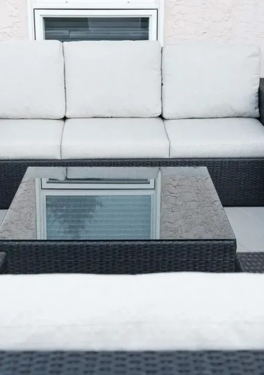 Outdoor patio with white-cushioned wicker seating, glass coffee table, and potted flowers