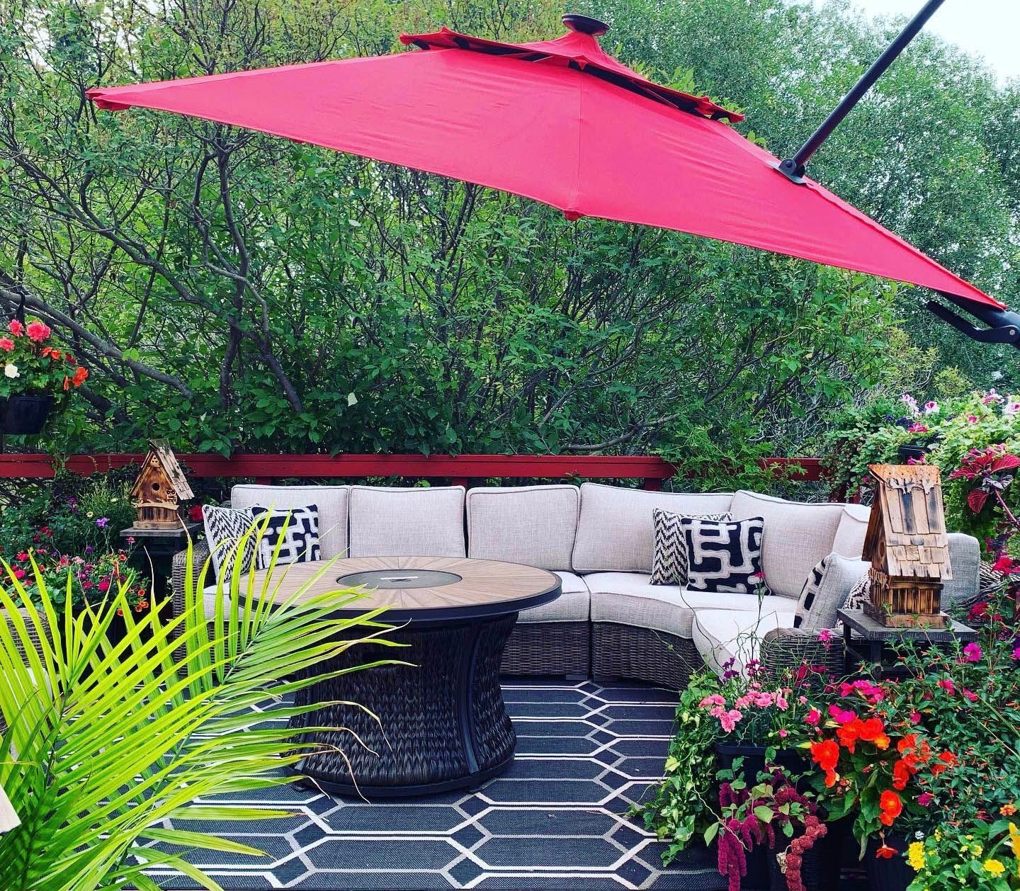 Patio lounge with curved white sofa, black table, red umbrella, and lush greenery and flowers