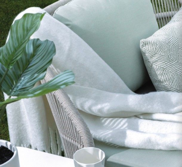 Mint green chair with white blanket, pillow, and potted plant in a soft, modern interior