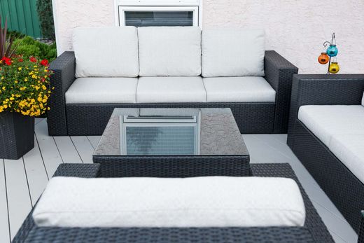 Outdoor patio with white-cushioned wicker seating, glass coffee table, and potted flowers