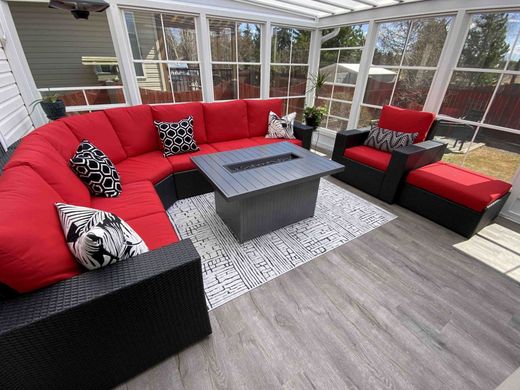Red and black sectional patio sofa around a gray coffee table in a bright sunroom with large windows.