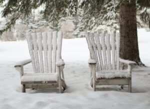 Two snow-covered wooden chairs beneath trees in a winter landscape
