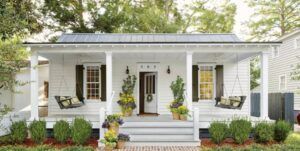 White bungalow-style house with a front porch, black shutters, potted plants, and a central front door