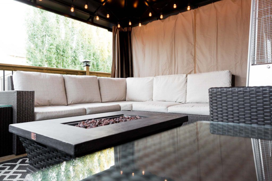 Modern outdoor lounge with white sectional sofa, glass table, and canopy lighting