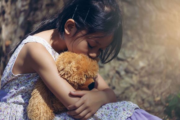 young girl hugging teddybear, seems scared