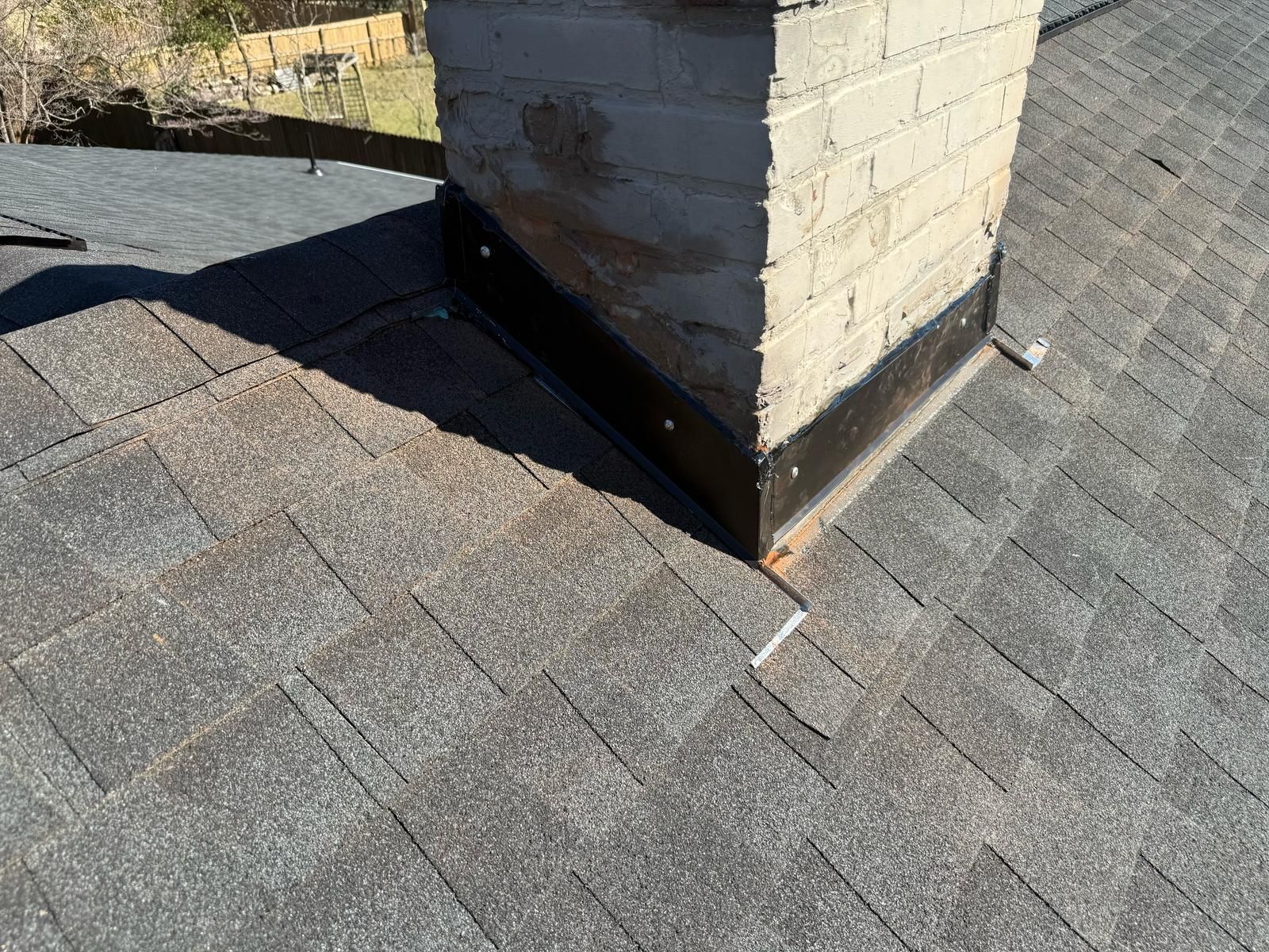 Brick chimney on a gray shingle roof, surrounded by metal flashing.