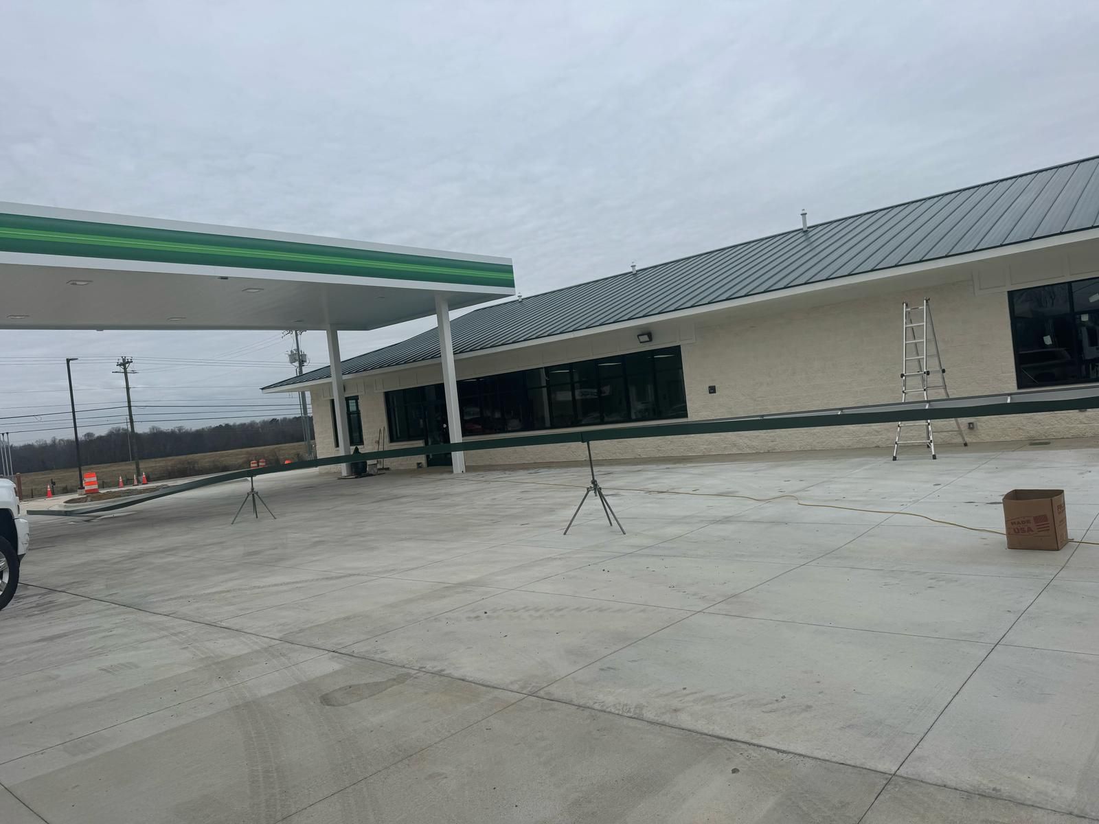 Gas station with green canopy and cream-colored building under cloudy sky. Concrete forecourt.