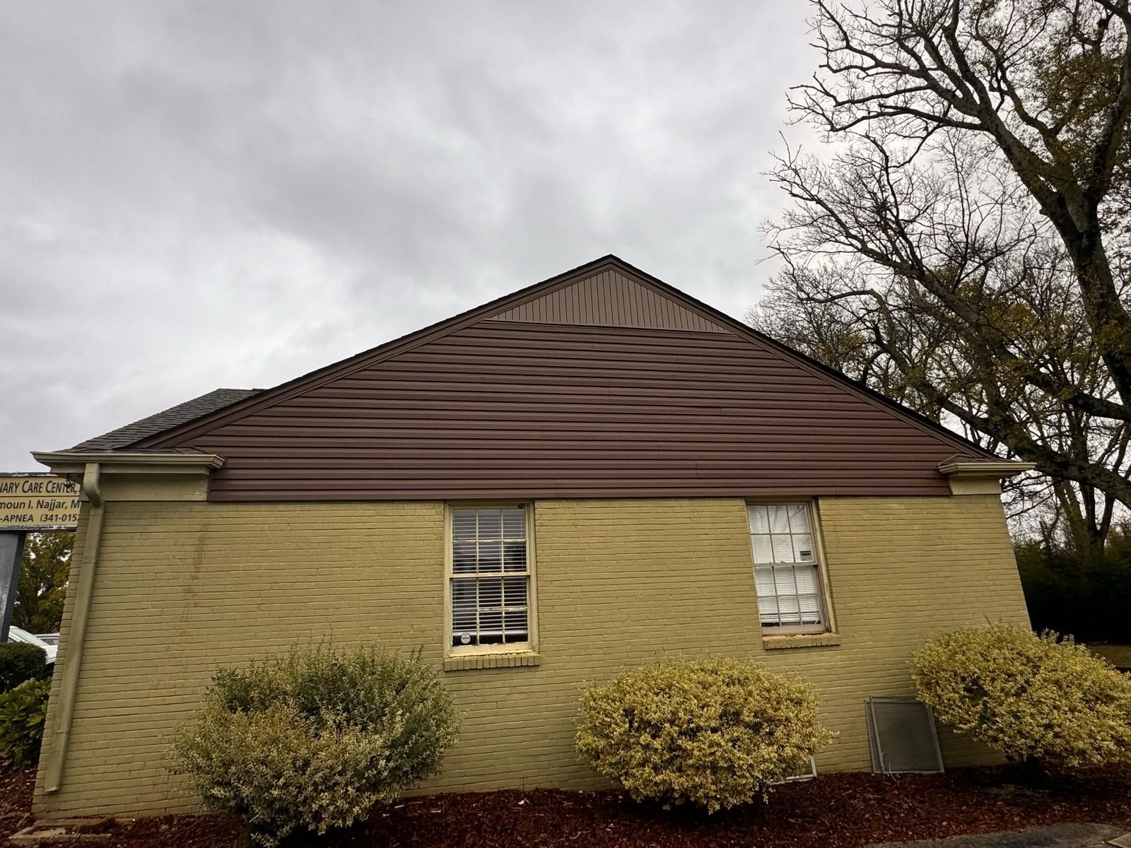Tan brick building with brown roof and two windows under a cloudy sky.