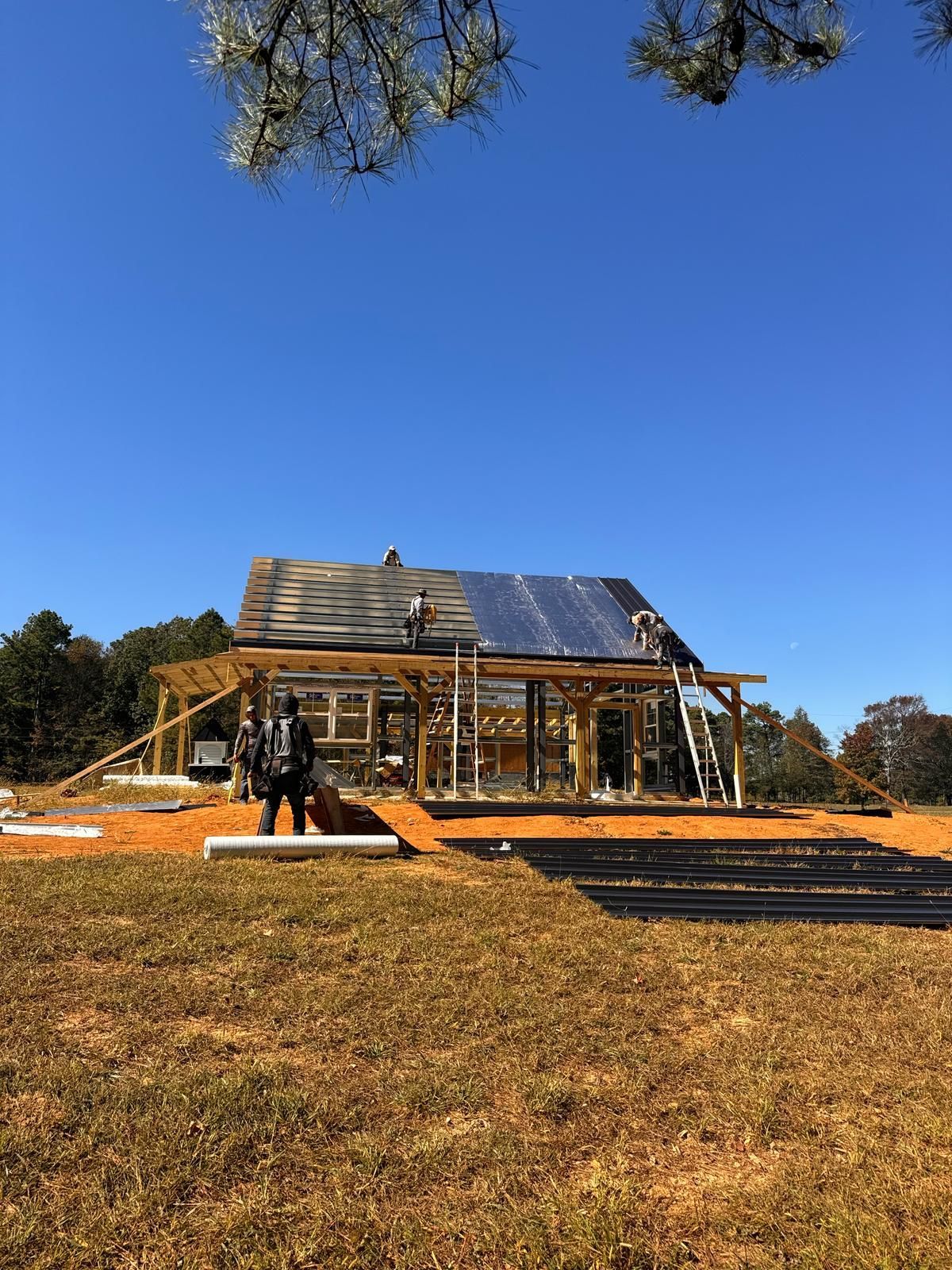 House under construction, workers on roof, blue sky, wooden frame structure.