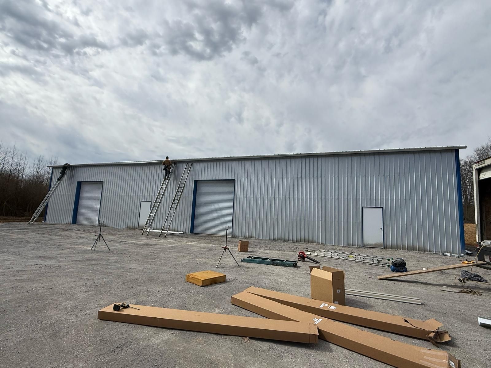 Exterior view of a metal building under construction, with open garage doors and tools on the ground.