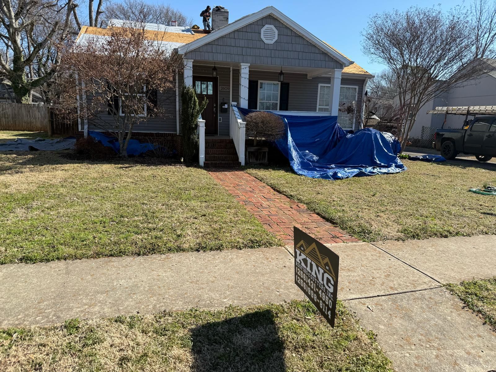 House under construction with blue tarp covering the porch, sign in yard.