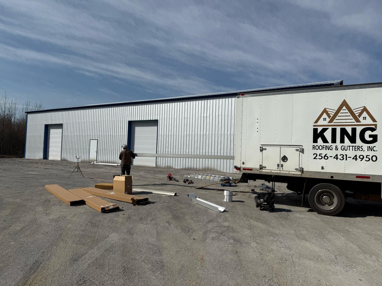 Building with KING ROOFS & GUTTERS truck; worker outside, supplies scattered.