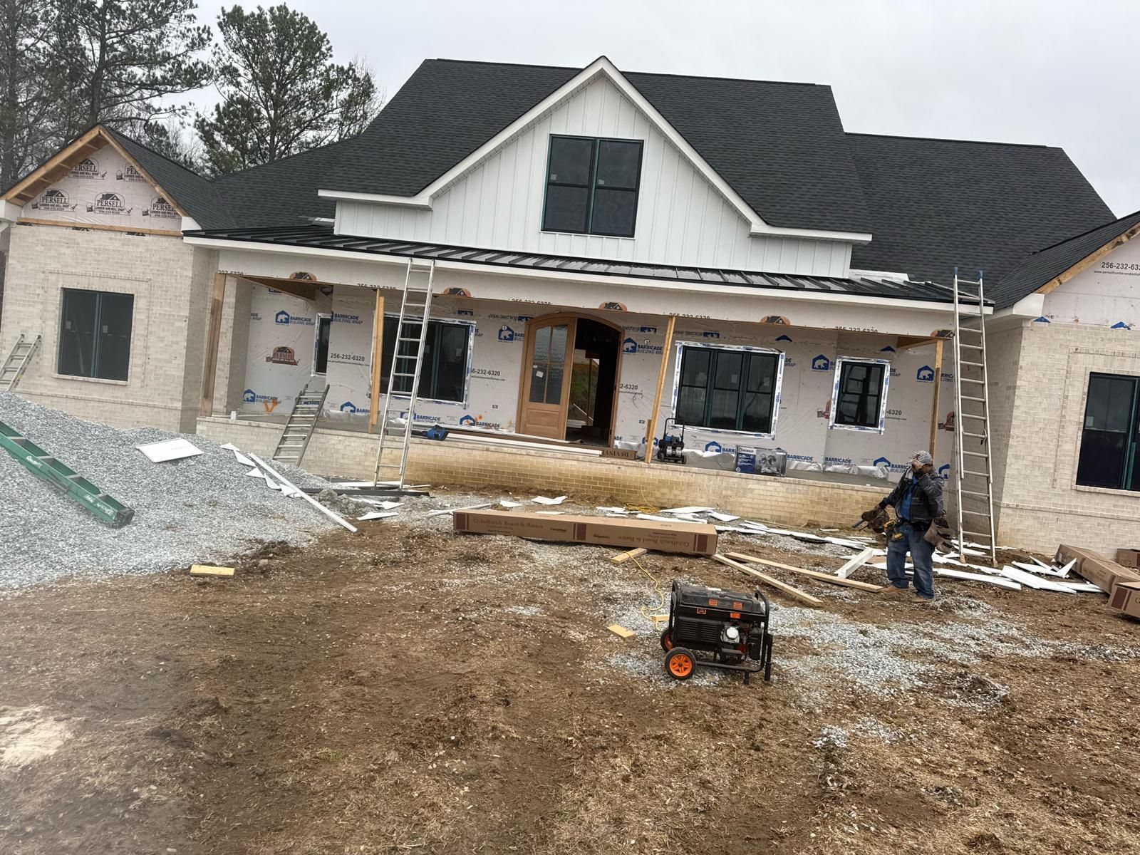 Construction of a two-story home with light brick, black roof, and workers present.