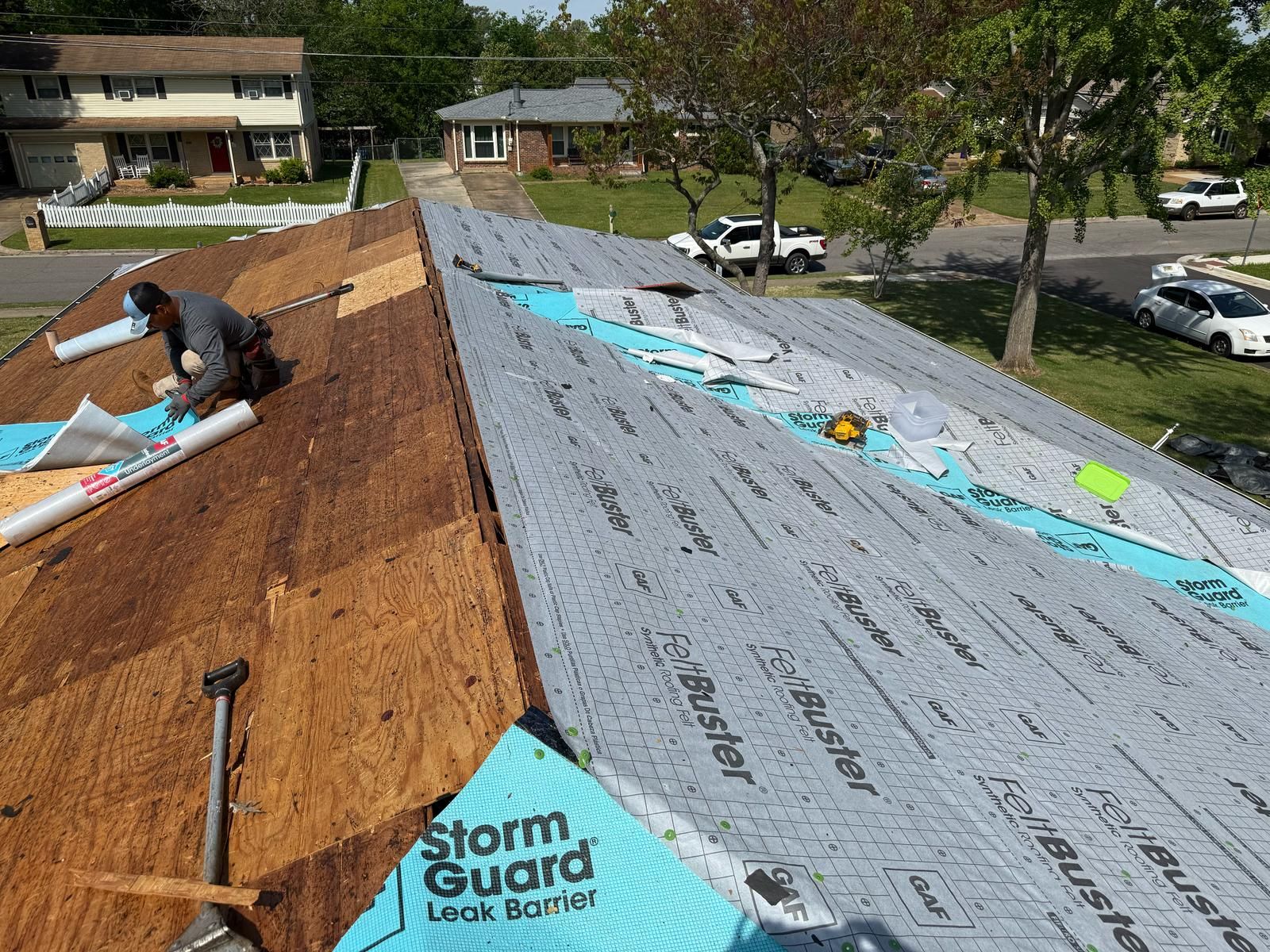 Roofer installing roofing underlayment on a house. Blue Storm Guard and gray roof paper visible.